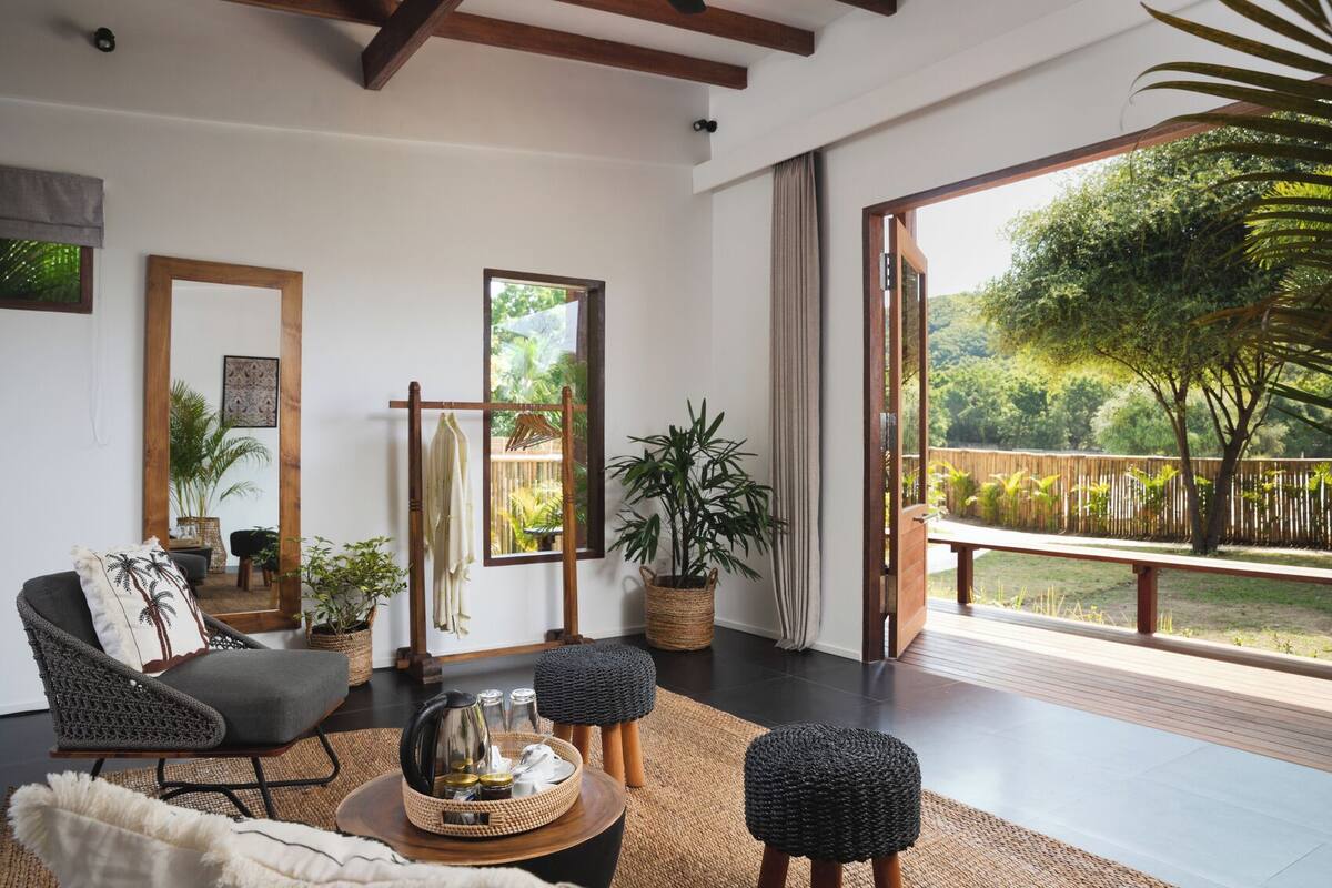 A modern living room with a large window, a sofa, a coffee table, and a view of a garden.