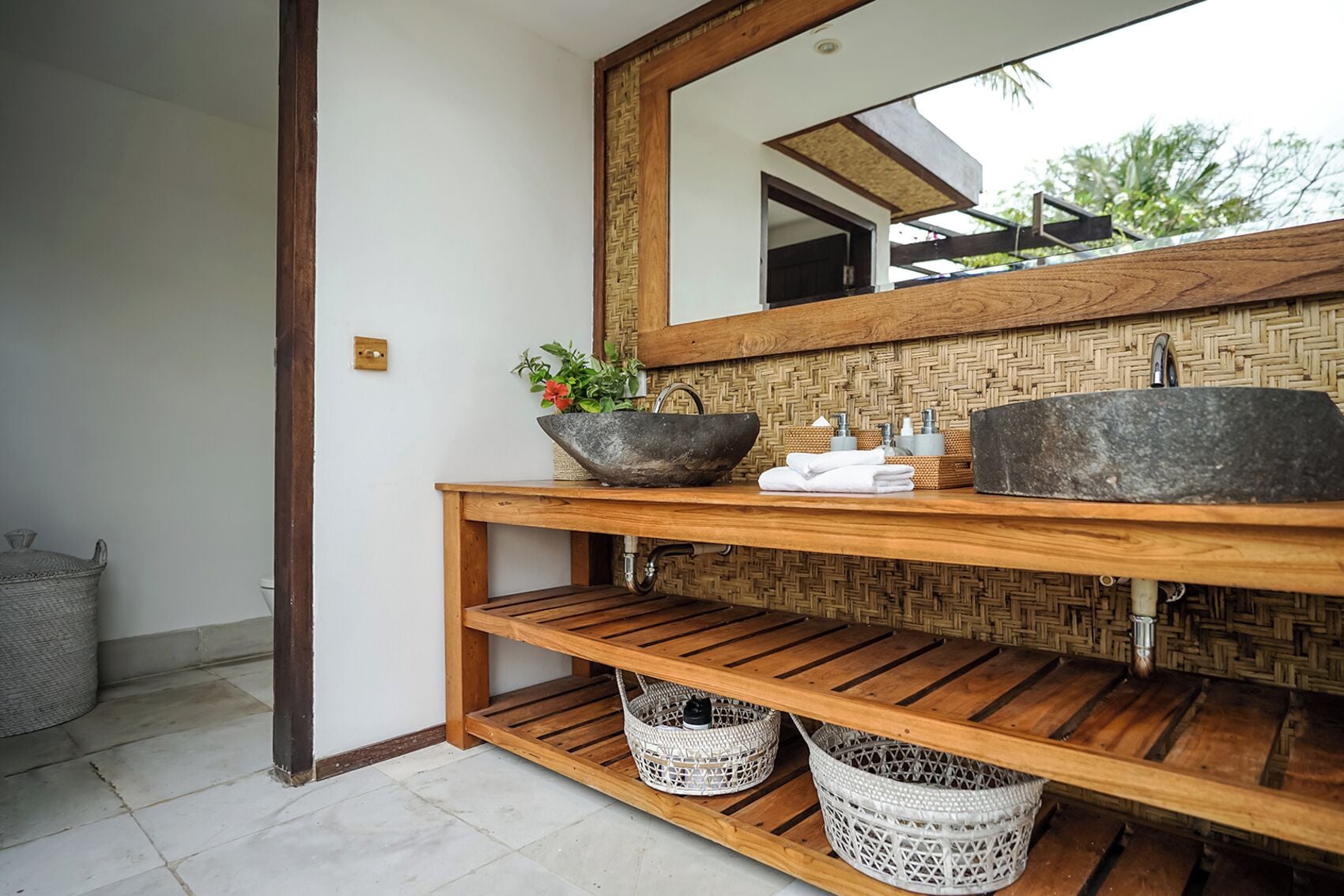 A bathroom with a wooden vanity, two stone sinks, a large mirror, and wicker baskets.
