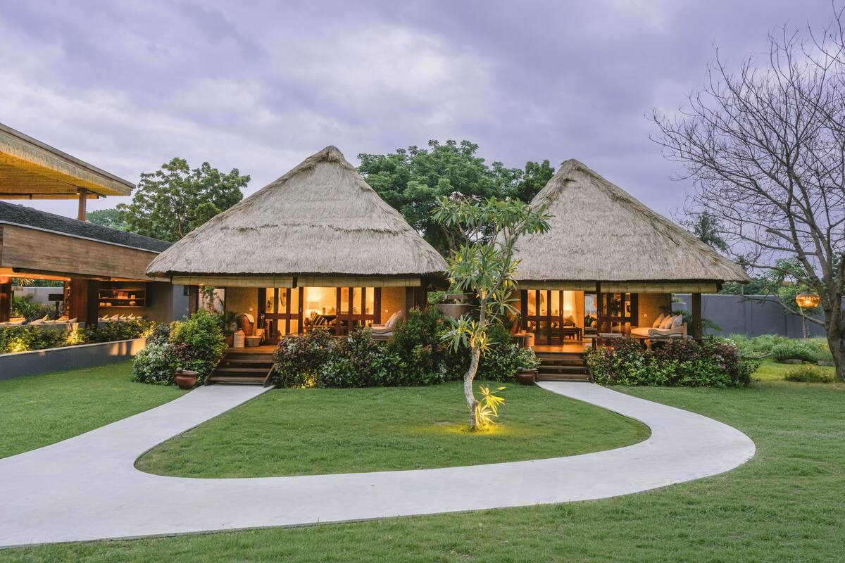 A resort with two thatched-roof structures, a well-maintained lawn, and a curved pathway.