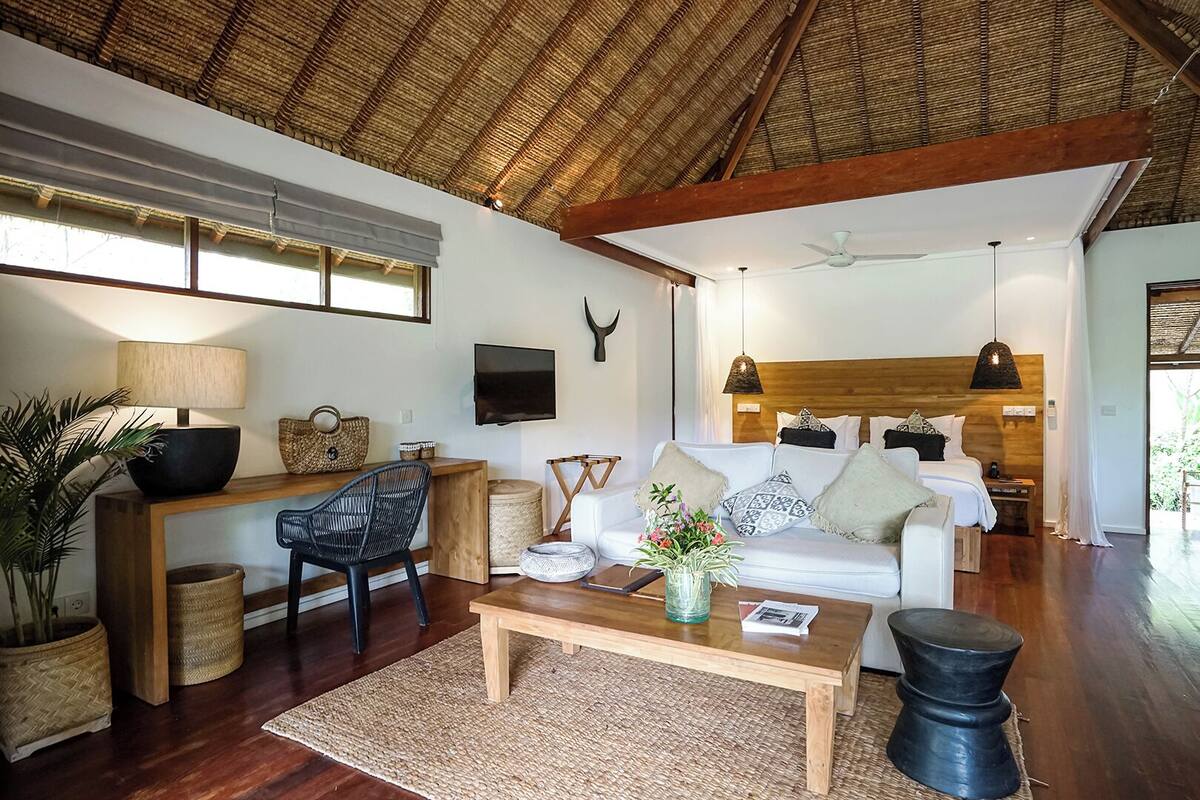 A spacious living area with a high ceiling, a wooden coffee table, a white sofa, a black chair, a TV, and a ceiling fan.