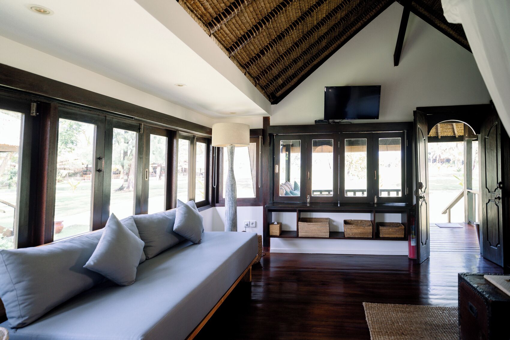 A spacious room with a large window, a sofa, a television, and a wooden ceiling.