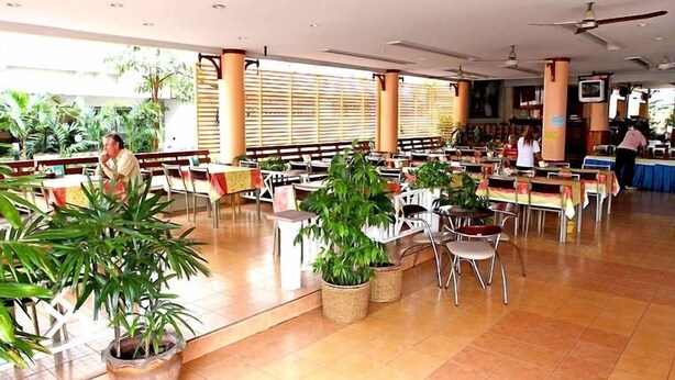 A spacious indoor dining area with multiple tables and chairs, potted plants, and a ceiling fan. - Queen Pattaya Hotel (Pattaya)