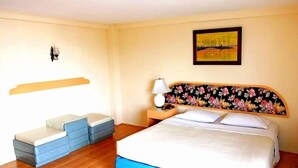 A hotel room with a bed, a nightstand, a lamp, a wall-mounted shelf, and a painting. - Queen Pattaya Hotel (Pattaya)