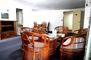 A dining area with wicker chairs and a table, a television on a cabinet, and a door in the background.