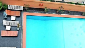 A swimming pool with a blue interior, surrounded by white lounge chairs and a wooden deck. - Queen Pattaya Hotel (Pattaya)