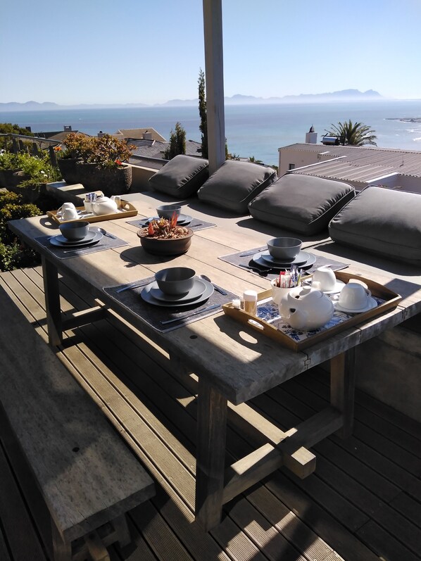 A wooden deck with a table set for breakfast overlooking the sea.