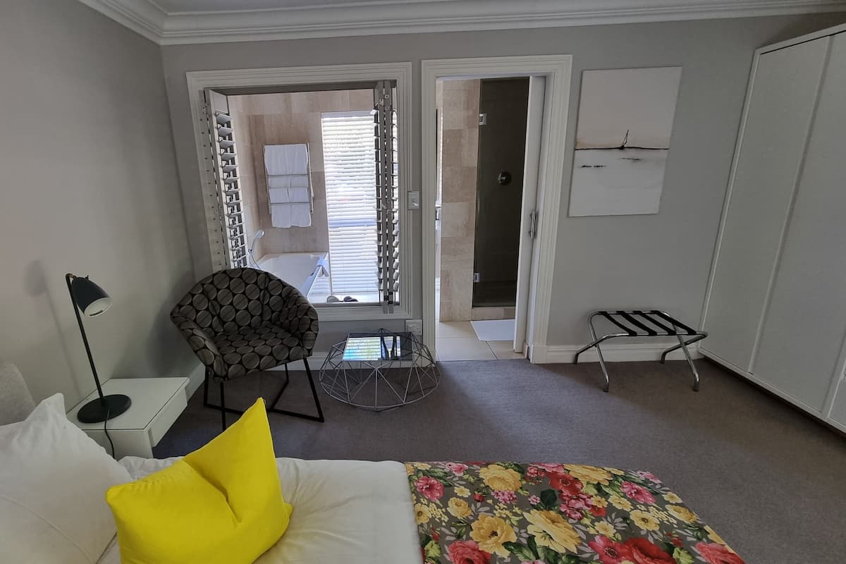 Una habitación de hotel con una cama, una silla, una mesita, una lámpara, un radiador y un armario.