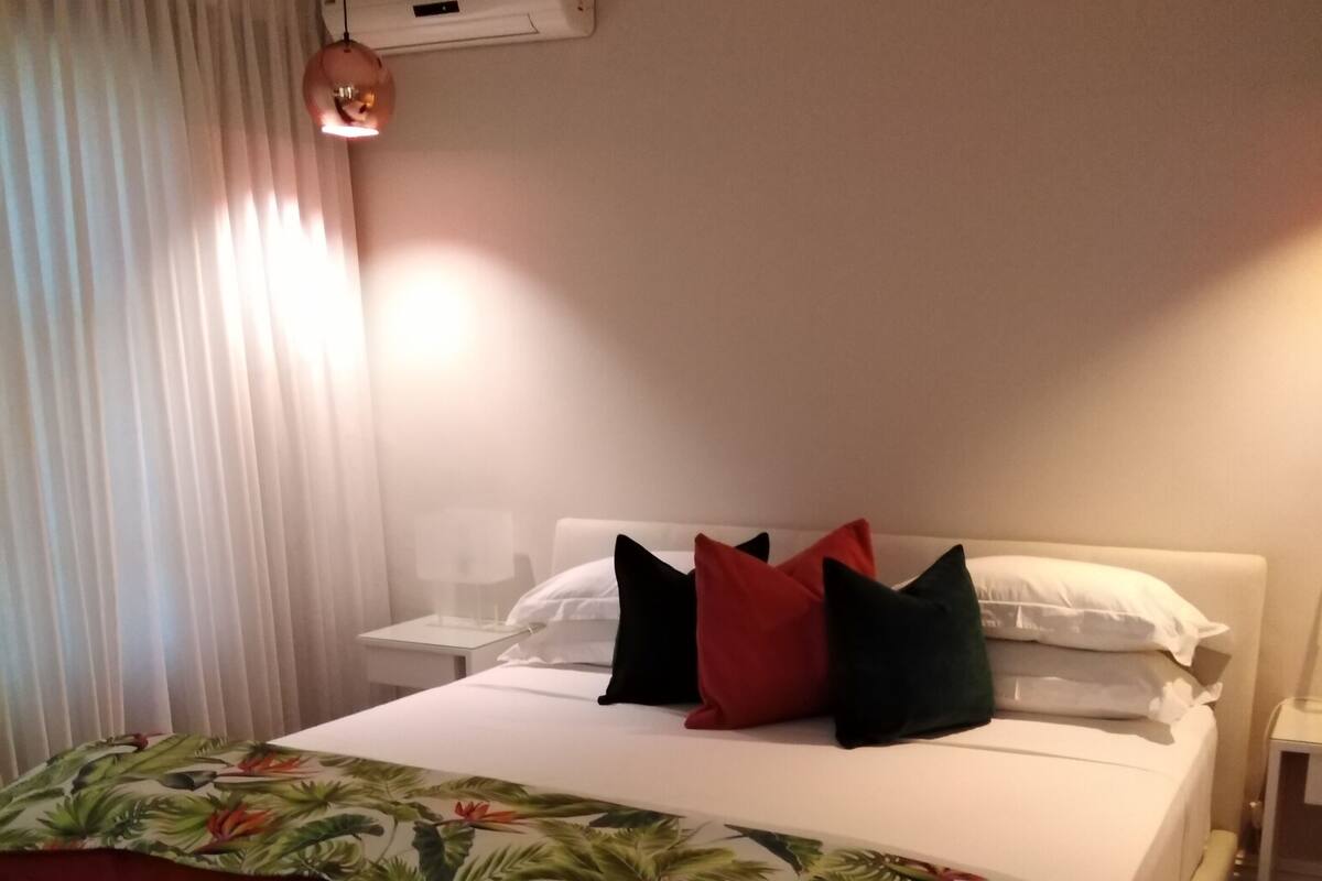Habitación de hotel con cama, mesita de noche, lámpara y ventana con cortinas.
