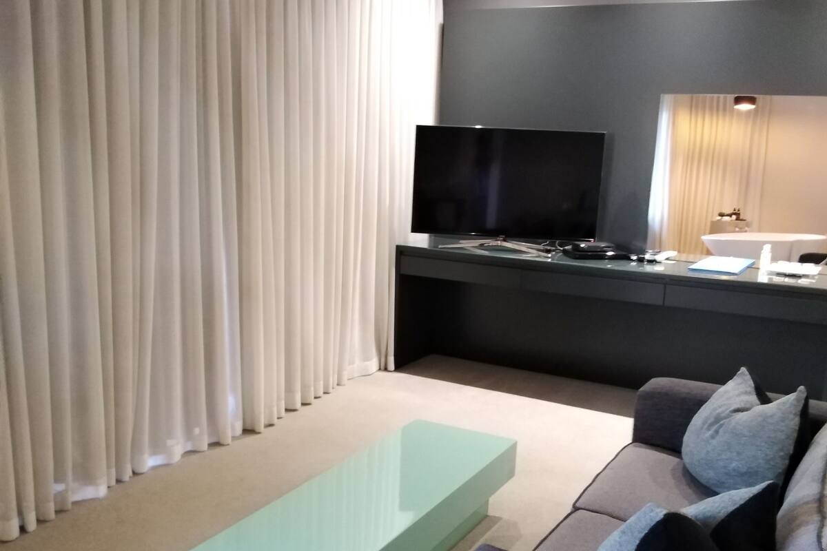 Una sala de estar moderna con un televisor de pantalla plana, un sofá, una mesa de centro y un comedor con una mesa y sillas.