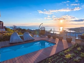 A pool area with a sunset view, lounge chairs, and potted plants.