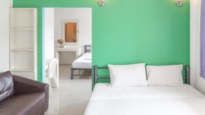 Habitación de hotel con cama, sofá de cuero marrón, armario blanco y baño visible a través de una puerta abierta.