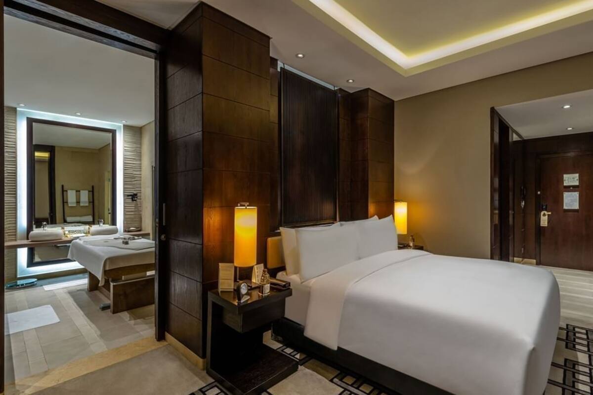 A modern hotel room with a large bed, bedside lamps, a nightstand, a mirror, and a view of the bathroom.