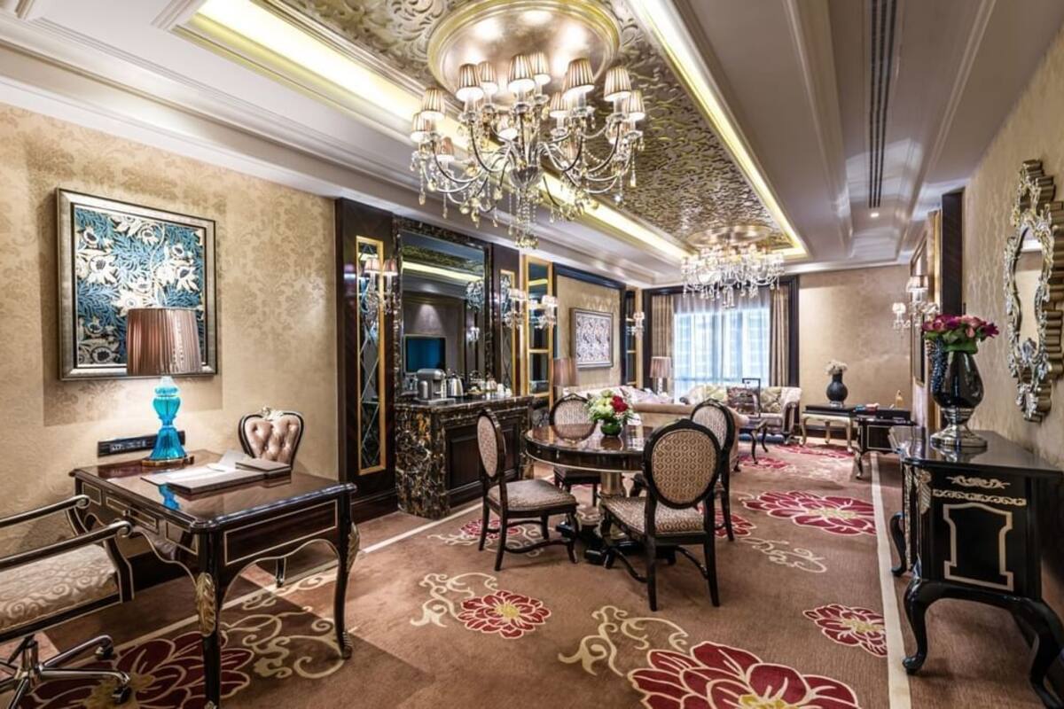 A luxurious hotel room with a large chandelier, ornate furniture, and a decorative mirror.