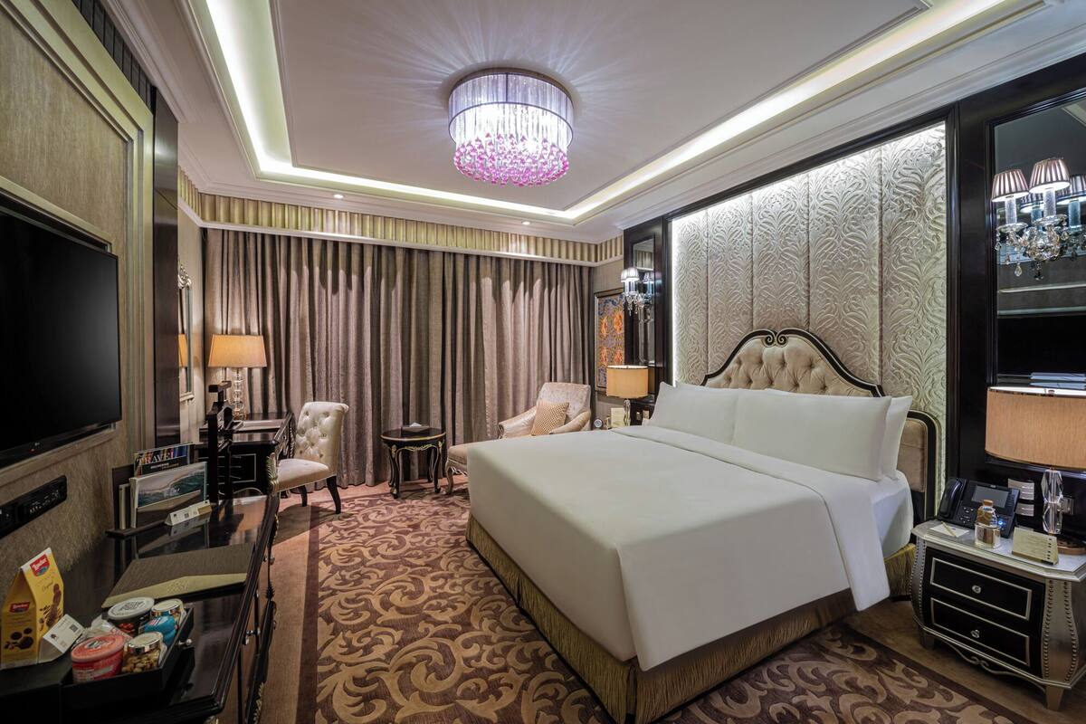 A hotel room with a large bed, a TV, a desk with a lamp, a chair, and a minibar.