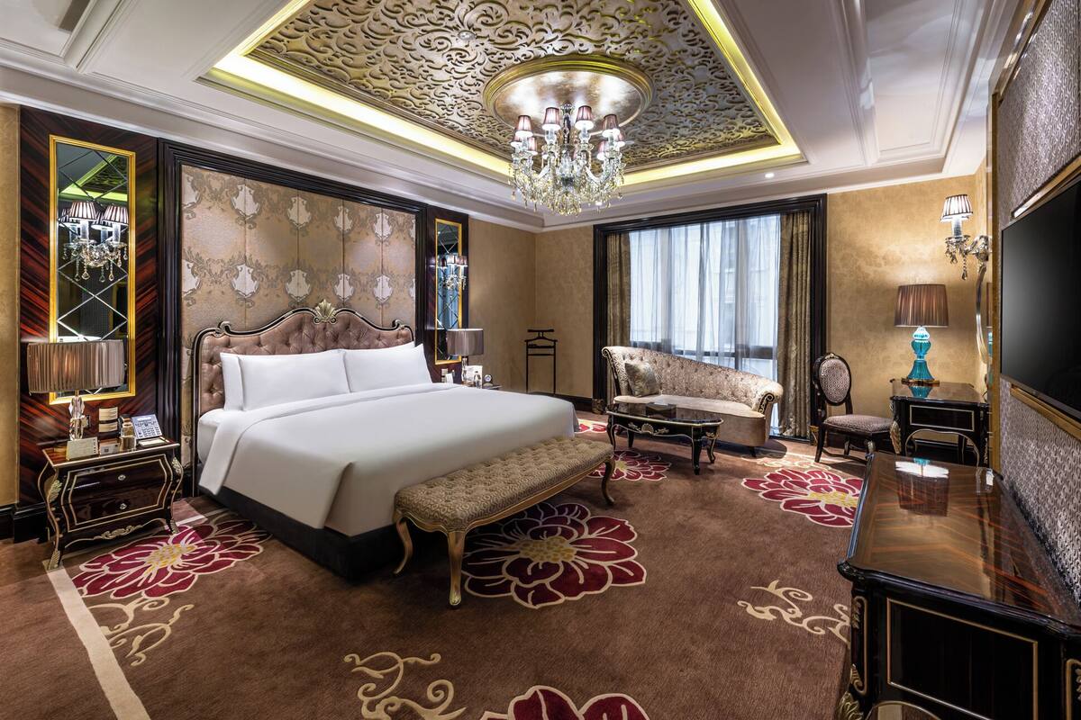 A luxurious hotel room with a large bed, a sofa, a TV, and a chandelier.