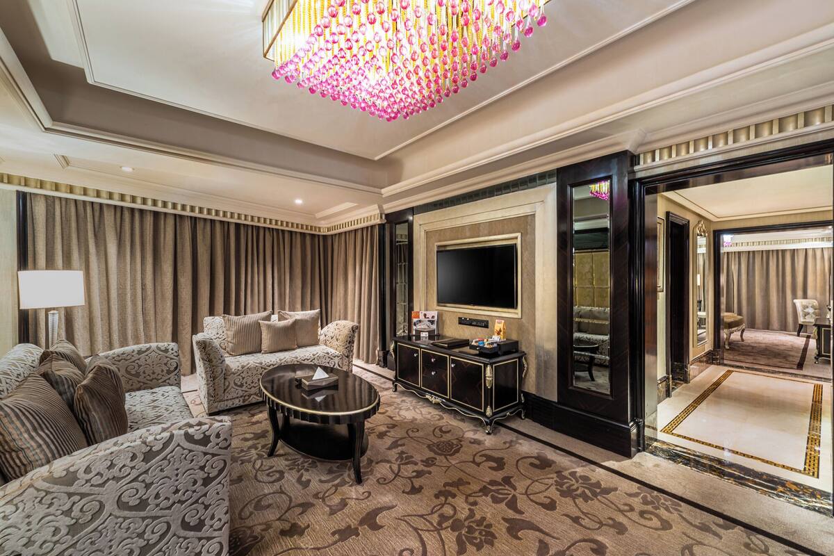 A luxurious living room with a patterned sofa, a coffee table, a TV, and a chandelier.