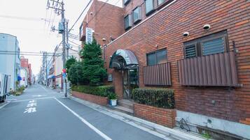 A narrow urban street lined with brick buildings, including a restaurant with a glass entrance and a small garden area.