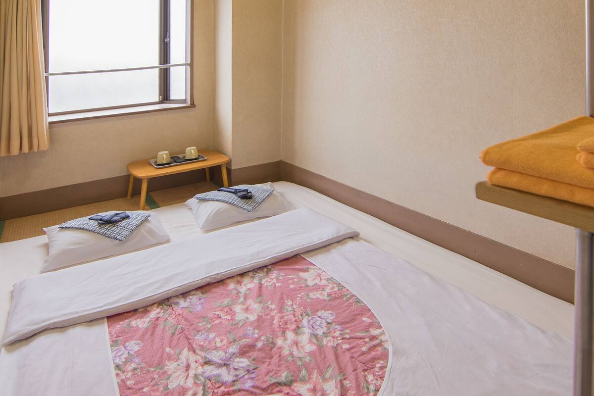 A hotel room with a bed, a small table with cups, and a window with curtains.