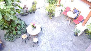 Une cour avec une table ronde et quatre chaises, entourée de plantes en pot et dotée d’un sol carrelé.