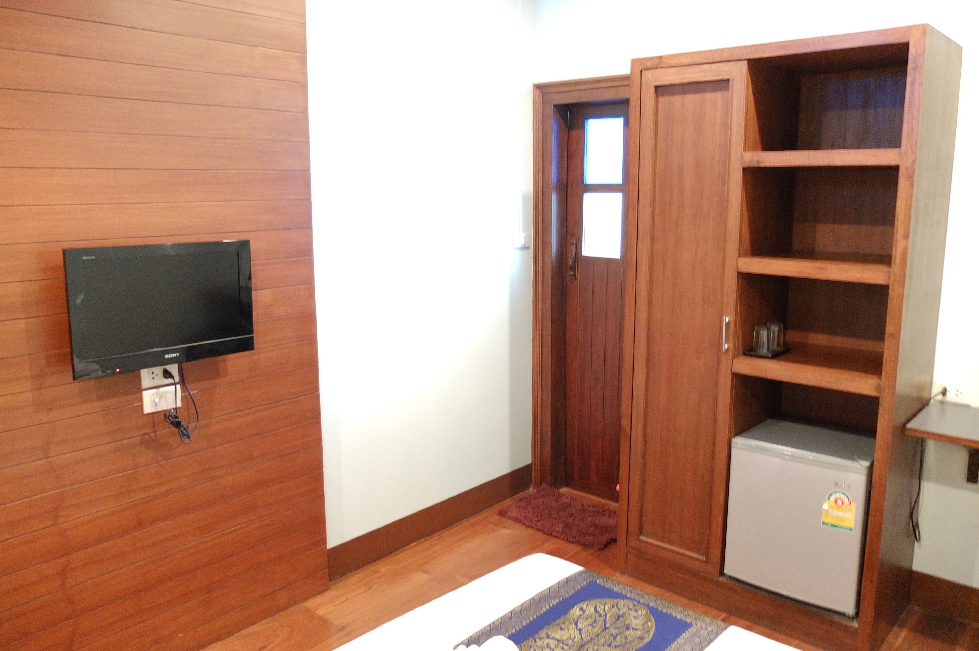 A room with a wooden wardrobe, a small refrigerator, and a mounted television.