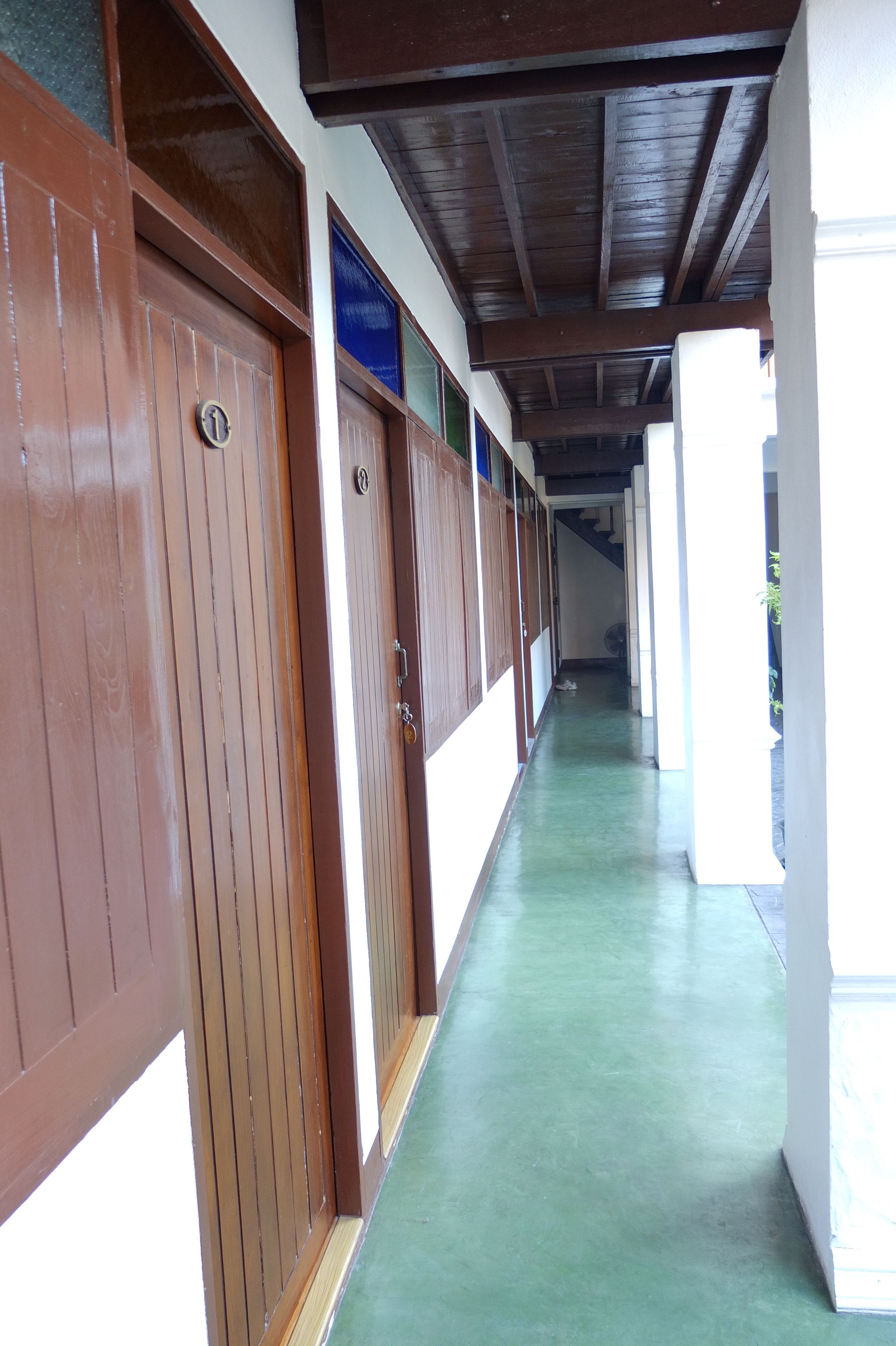 A corridor with wooden doors and a green floor, leading to a staircase.