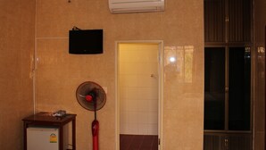 A room with beige walls, a ceiling fan, an air conditioner, a television, and a door leading to another room. - Lucky 1 Guesthouse (Phnom Penh)
