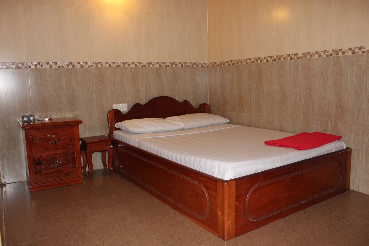 A neatly made bed with a wooden headboard, a wooden nightstand with drawers, and a red towel on the bed.