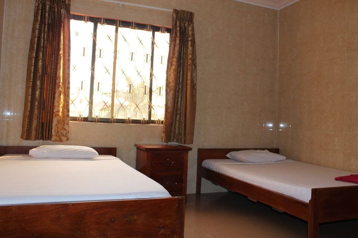 A room with two wooden beds, a wooden nightstand, and a window with curtains.