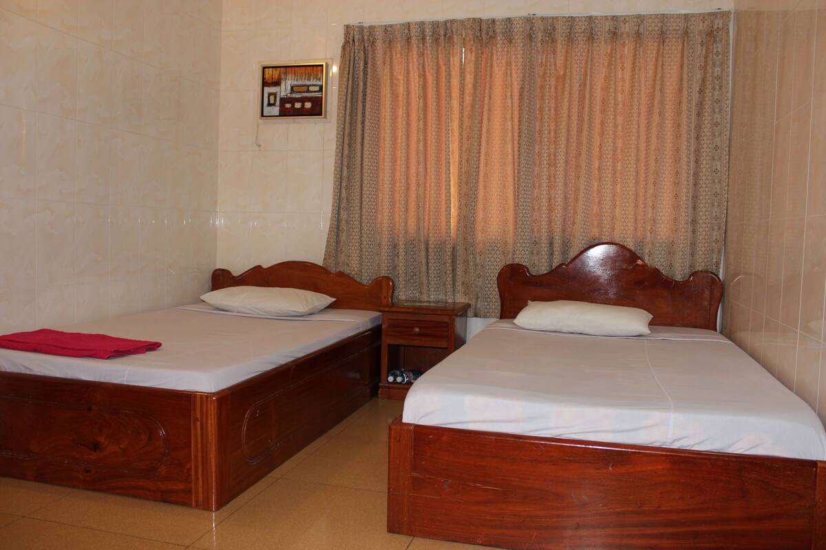 A room with two wooden beds, a nightstand, a framed picture on the wall, and a patterned curtain.