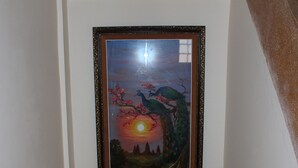 Cuadro enmarco de una escena de atardecer con un pavo real y un árbol, sobre una pared blanca encima de una escalera de madera.