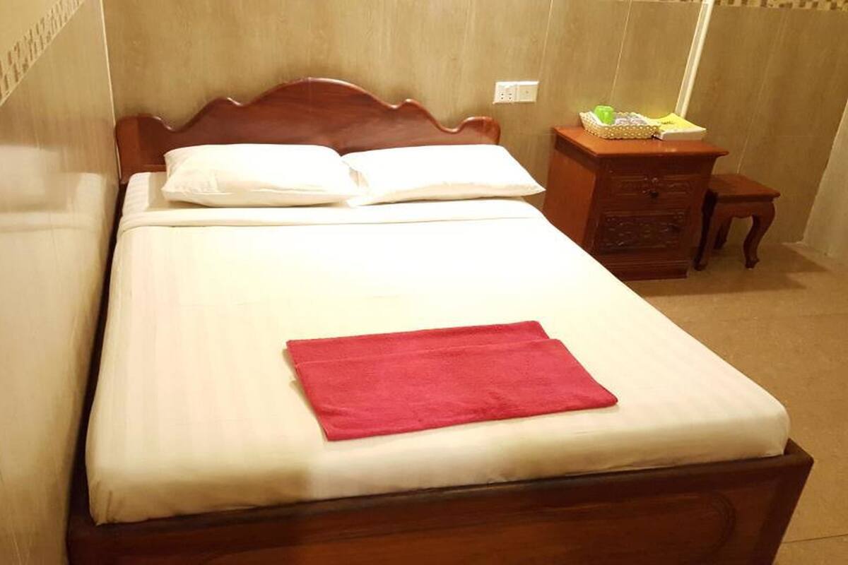 Una cama bien hecha con una toalla roja, un cabecero de madera y una mesita de noche de madera con una cesta verde.
