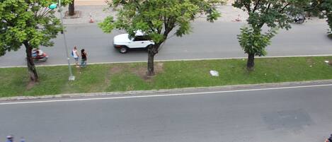 Vista callejera con árboles, un coche blanco y una motocicleta azul.