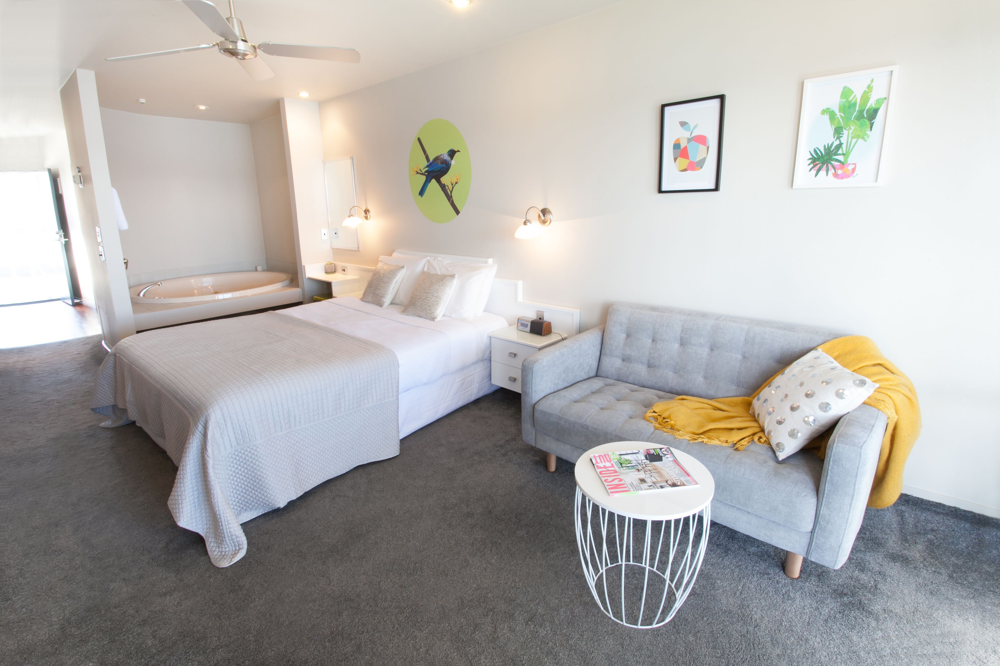 A modern hotel room with a bed, a sofa, a small round table, and a ceiling fan.