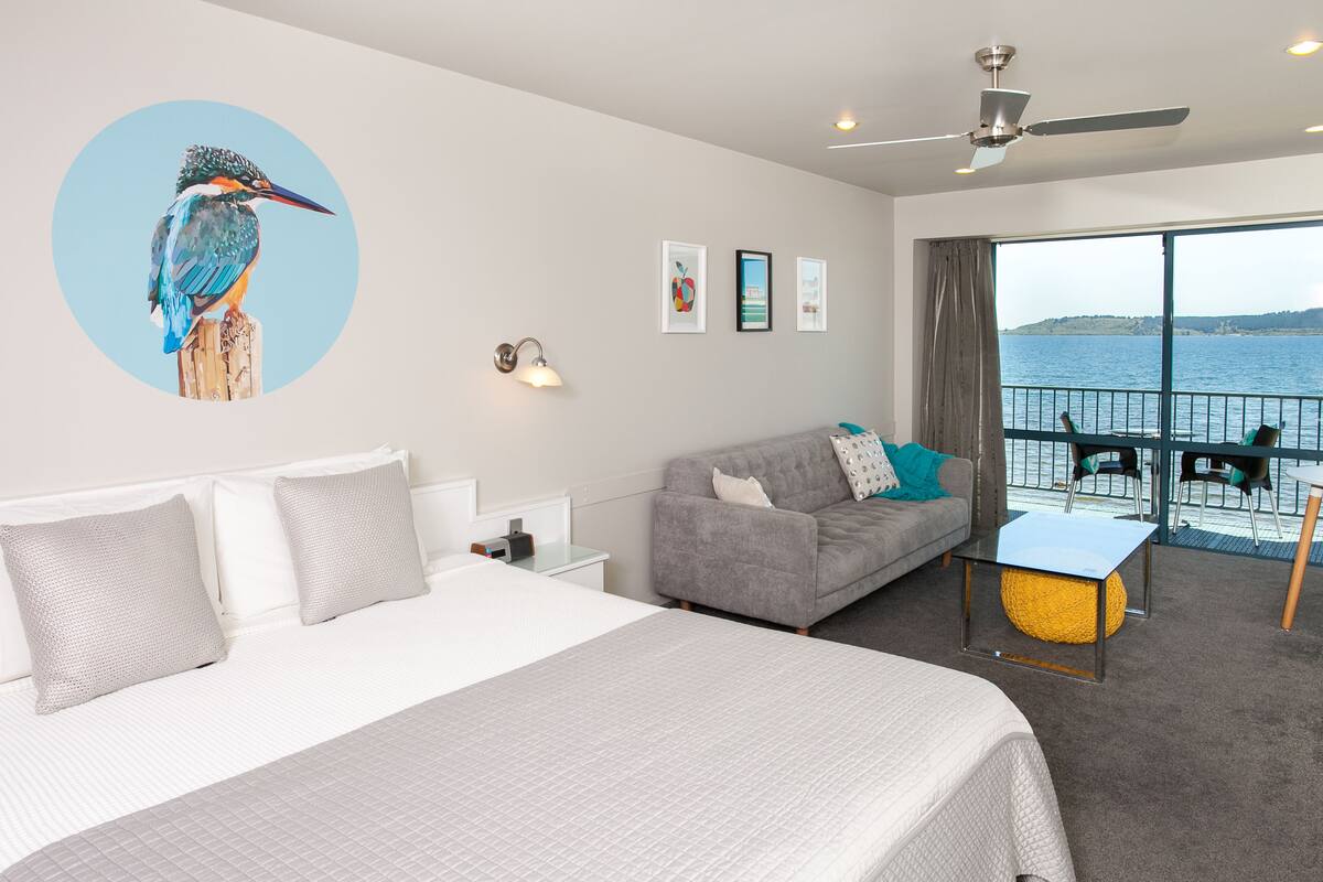 A hotel room with a bed, a sofa, a balcony with a view of the sea, and a ceiling fan.