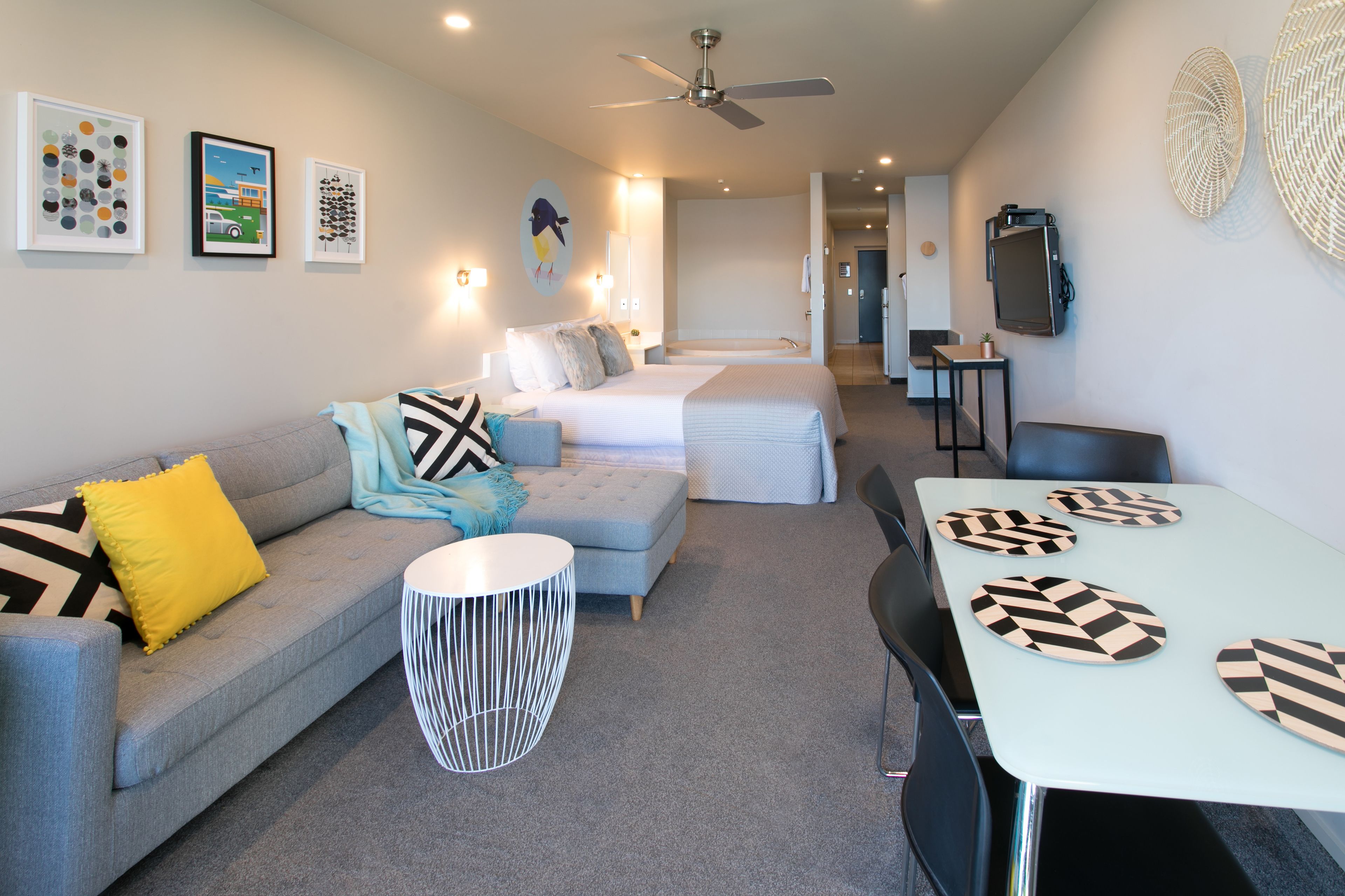 A modern hotel room with a sofa, two beds, a dining table, and a ceiling fan.