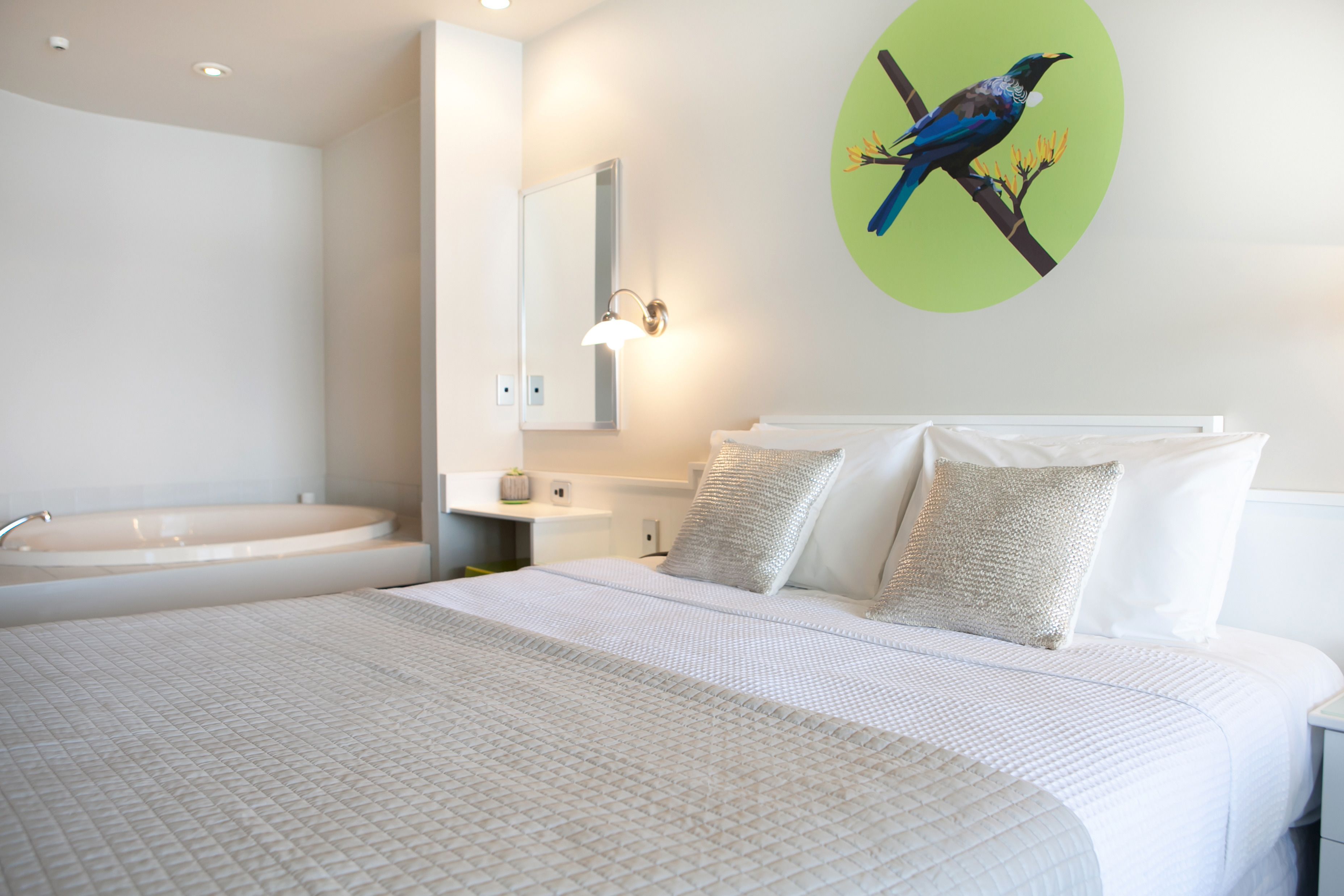 A hotel room with a large bed, a bathroom with a bathtub, and a wall-mounted mirror.