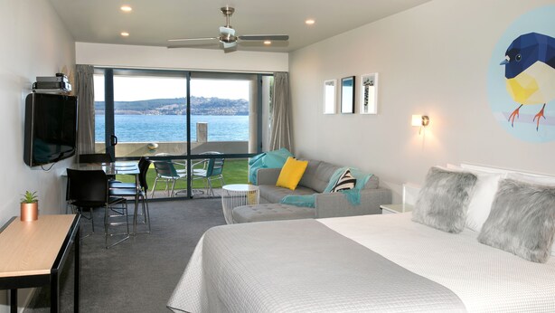 A modern hotel room with a large bed, a sofa, a dining area, and a balcony with a view of the sea. - Boulevard Waters (Taupo)