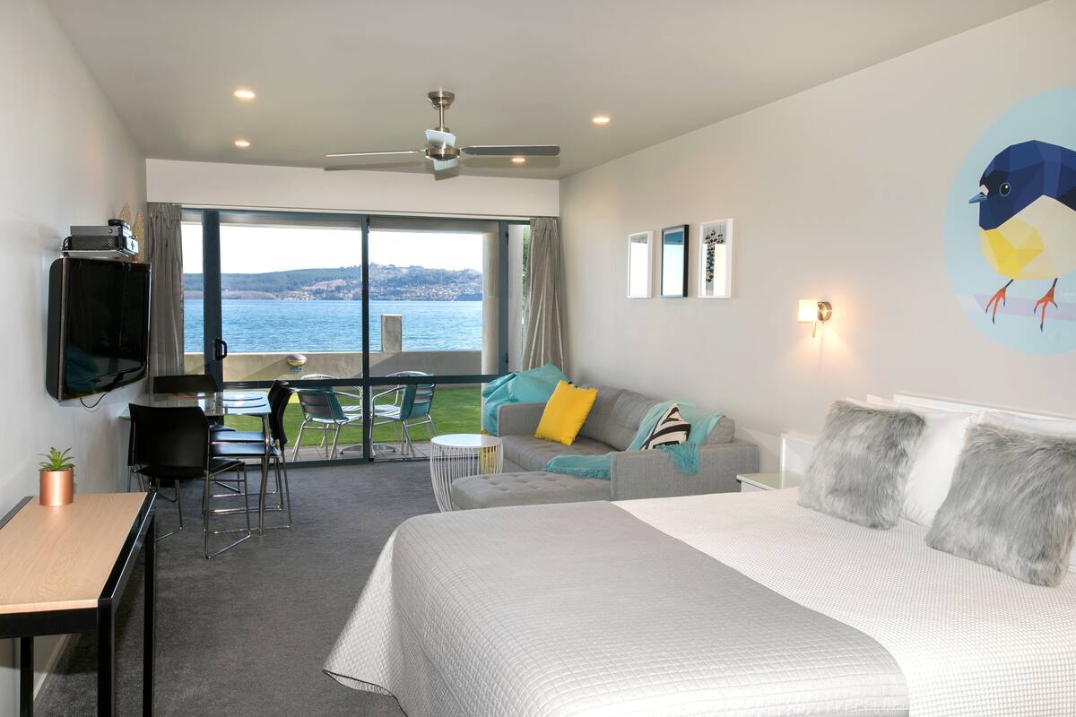 A modern hotel room with a large bed, a sofa, a dining area, and a balcony with a view of the sea.