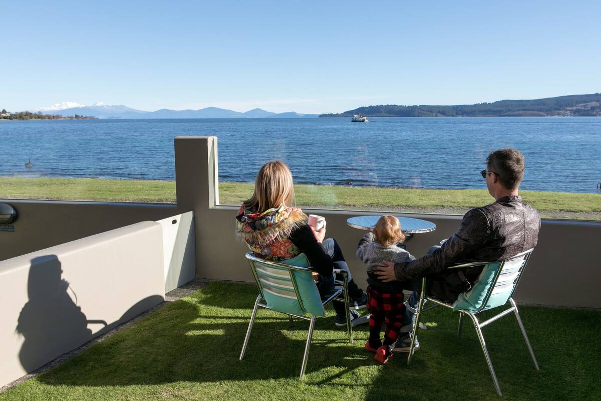 A terrace with a view of a lake, a table, and chairs.