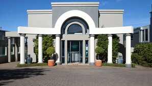 A modern building with a central arched entrance, flanked by columns, and surrounded by potted plants. - Boulevard Waters (Taupo)