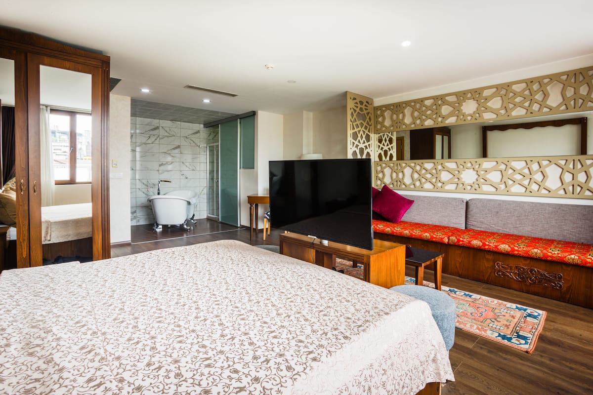 Une chambre avec un grand lit, une télévision, un canapé et une salle de bain avec une baignoire.
