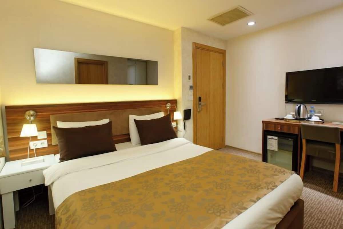 Une chambre d’hôtel comprenant un lit, une table de chevet, une lampe, une télévision et un petit bureau avec une chaise.