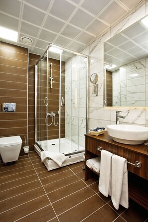 Een moderne badkamer met een douchecabine van glas, een witte wastafel en een houten wastafelmeubel.