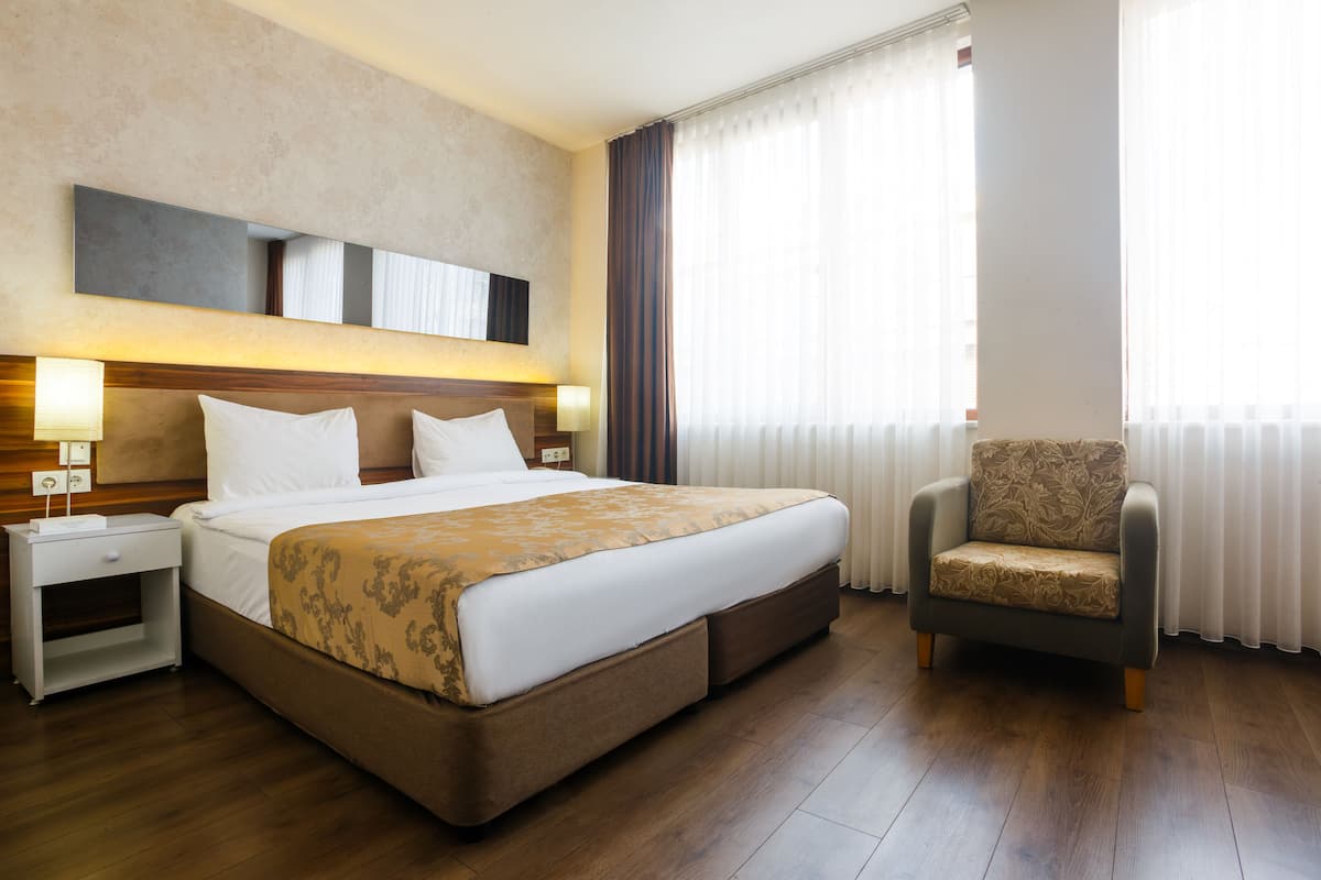 Une chambre d’hôtel avec un grand lit, une table de chevet, une chaise et une fenêtre avec des rideaux.