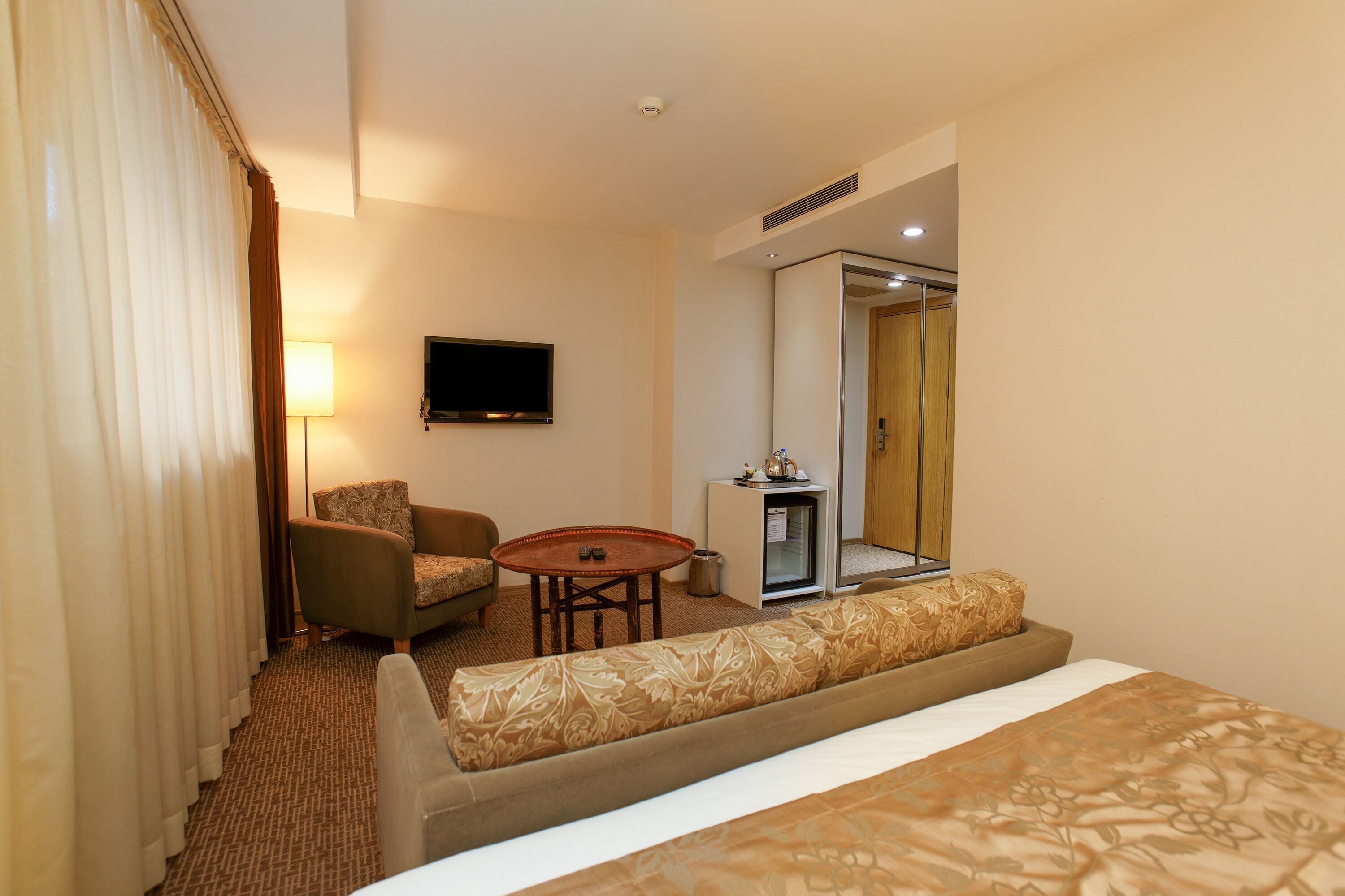 A hotel room with a bed, a sofa, a small table, a TV, and a door leading to a bathroom.