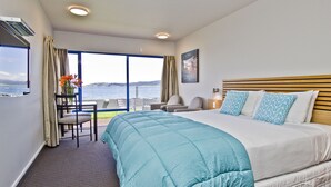 Habitación de hotel con una cama grande, vista al mar, zona de comedor con mesa y sillas, y una ventana con cortinas.