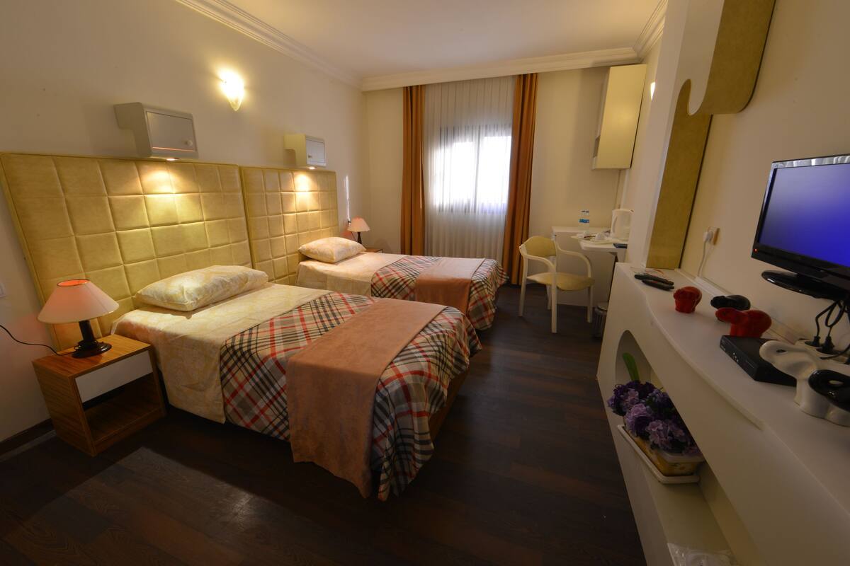 A hotel room with two beds, a desk, a chair, a television, and a small table with a lamp.