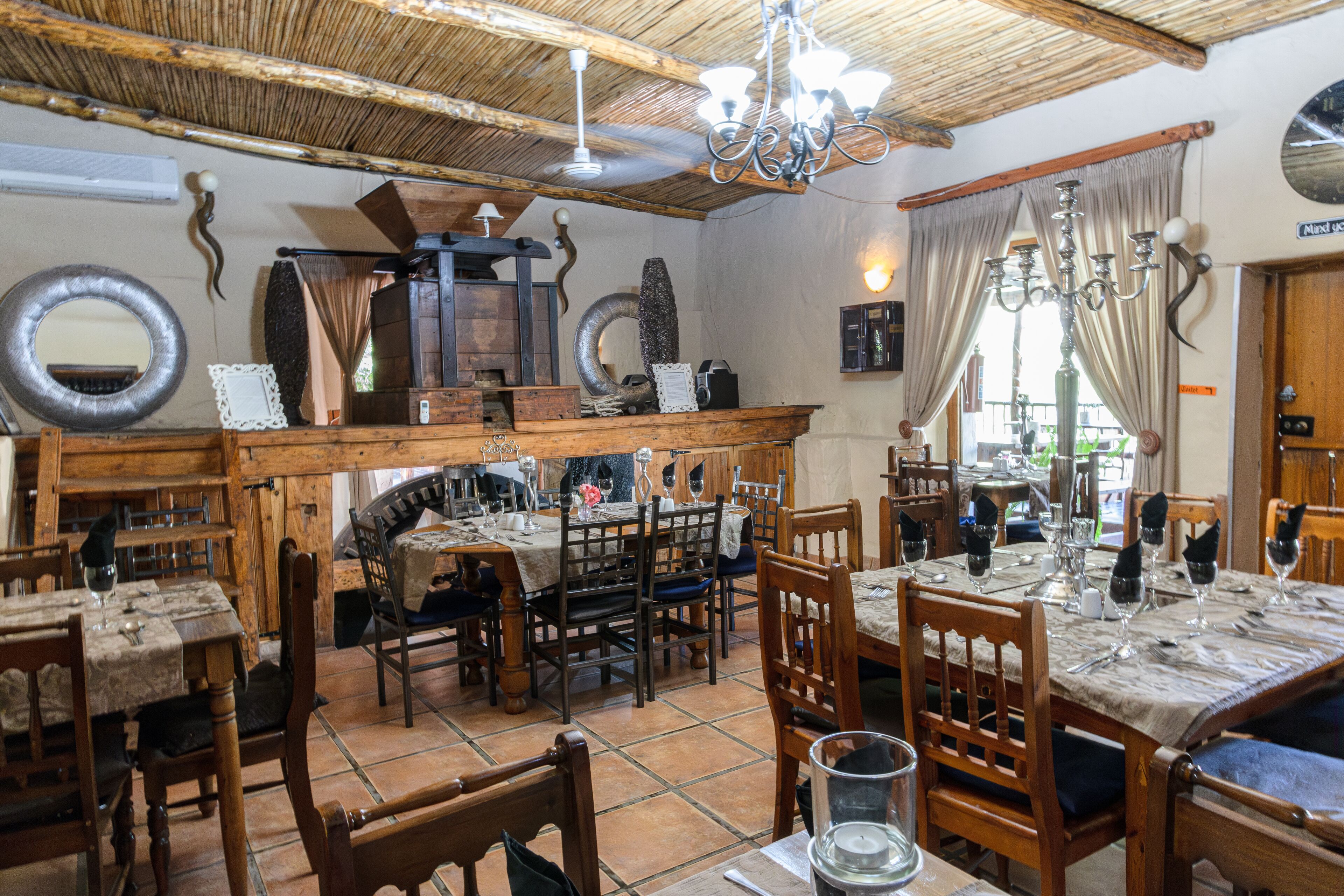 A rustic dining area with wooden tables and chairs, a chandelier, and a rustic ceiling.
