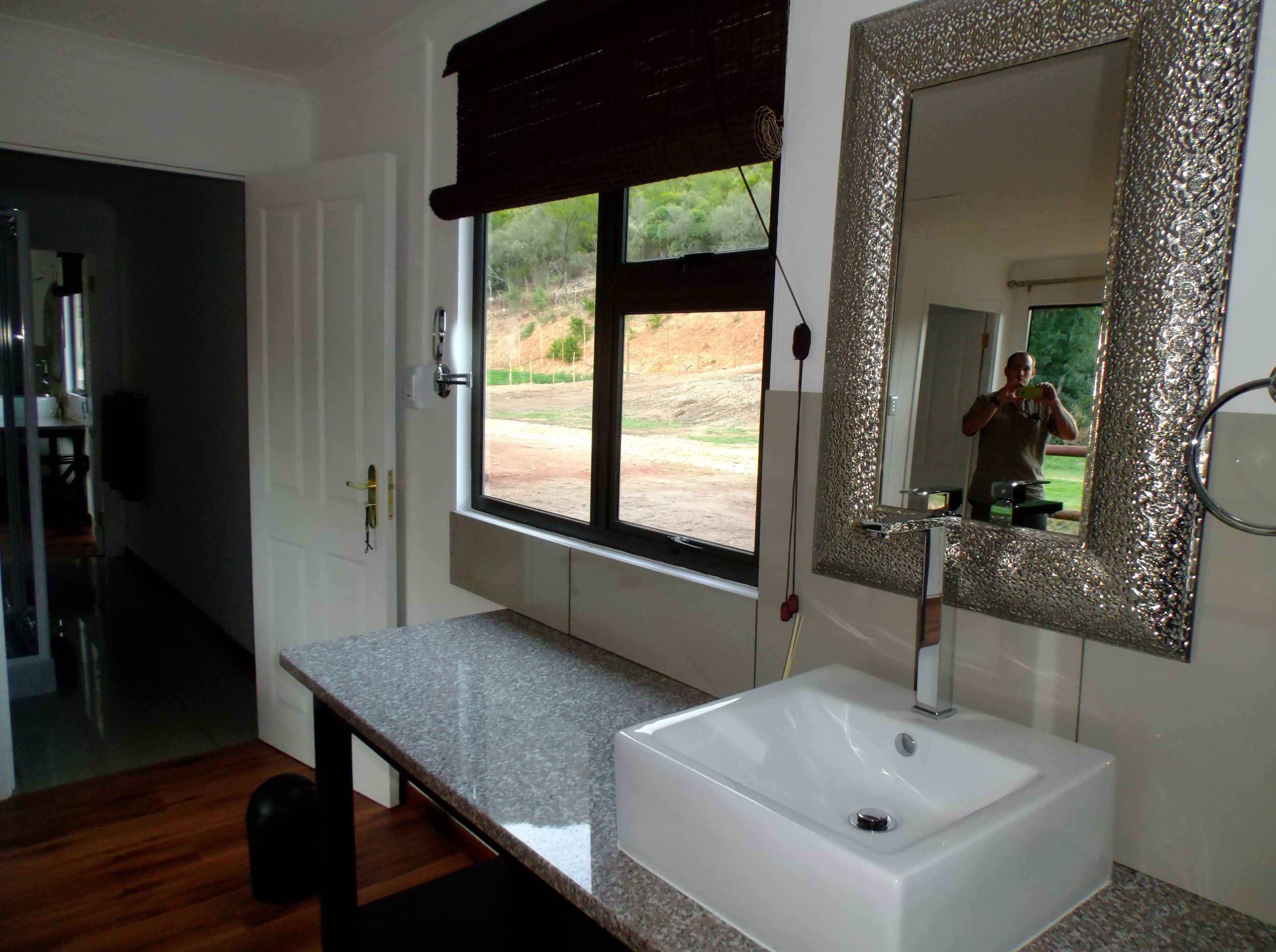 A bathroom with a white sink, a large mirror with a textured frame, and a window with a view of the outdoors.