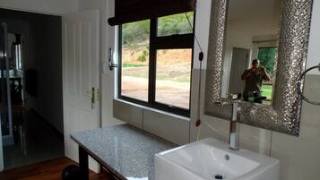 A bathroom with a white sink, a large mirror with a textured frame, and a window with a view of the outdoors.